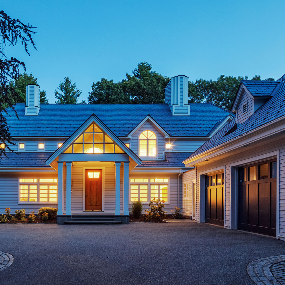 2-story house with blue paneling and warm indoor lighting at sunset