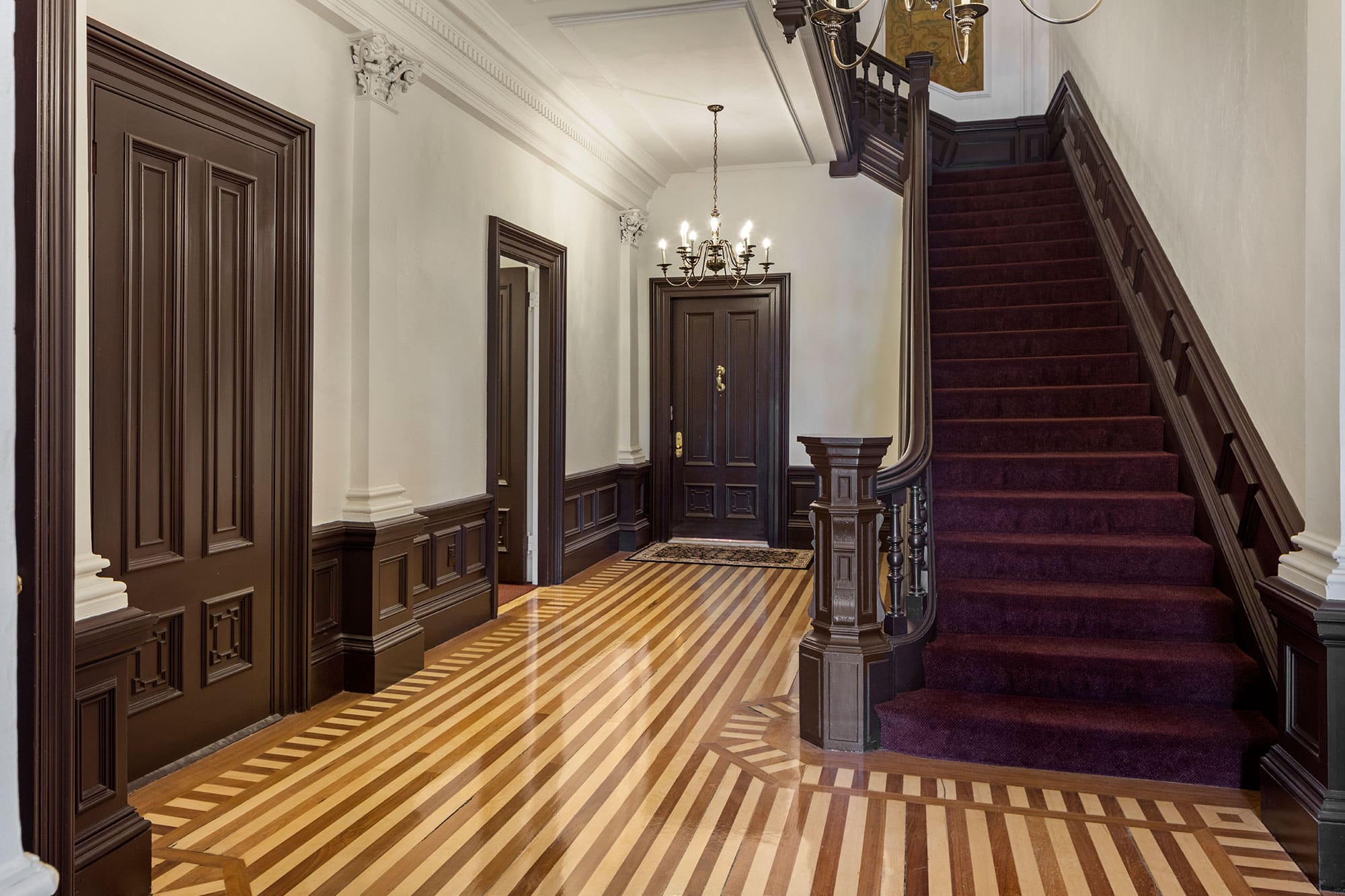 Home foyer with decorative striped wood floors and carpeted staircase